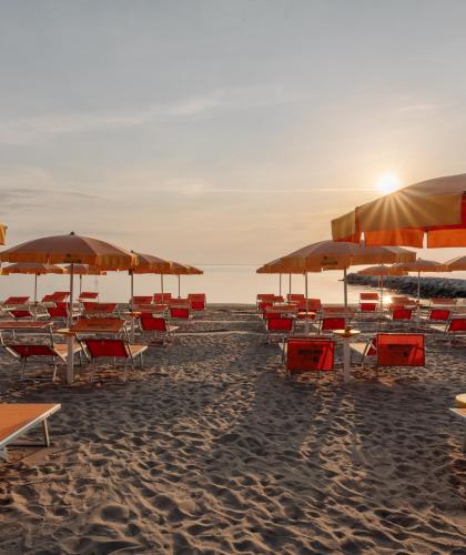 Spiaggia al tramonto con ombrelloni e lettini arancioni.