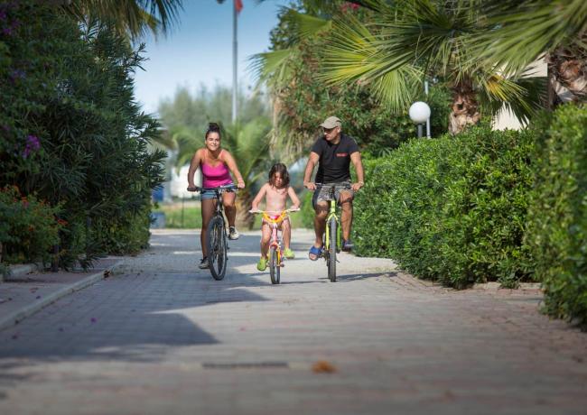 Famiglia in bicicletta su un sentiero alberato, giornata soleggiata e rilassante.