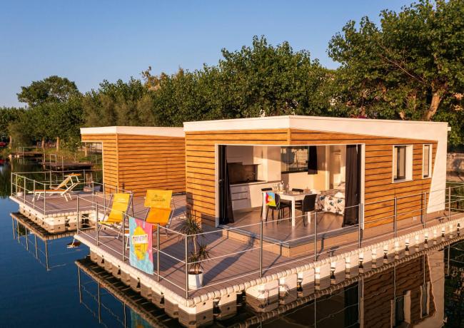 Casa galleggiante moderna con terrazza sul lago, circondata da alberi.