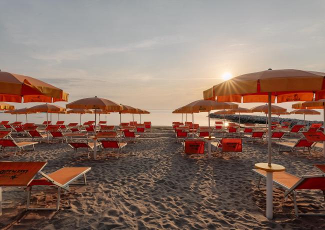 Spiaggia al tramonto con ombrelloni e lettini arancioni.