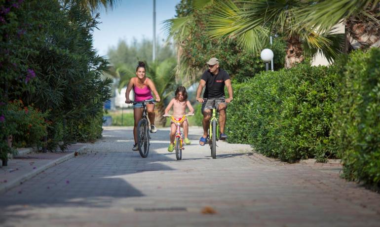 Famiglia in bicicletta su un sentiero alberato, giornata soleggiata e rilassante.