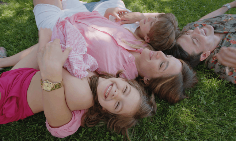 Famiglia felice sdraiata sull'erba, sorridente e rilassata.