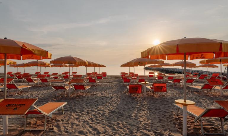 Spiaggia al tramonto con ombrelloni e lettini arancioni.