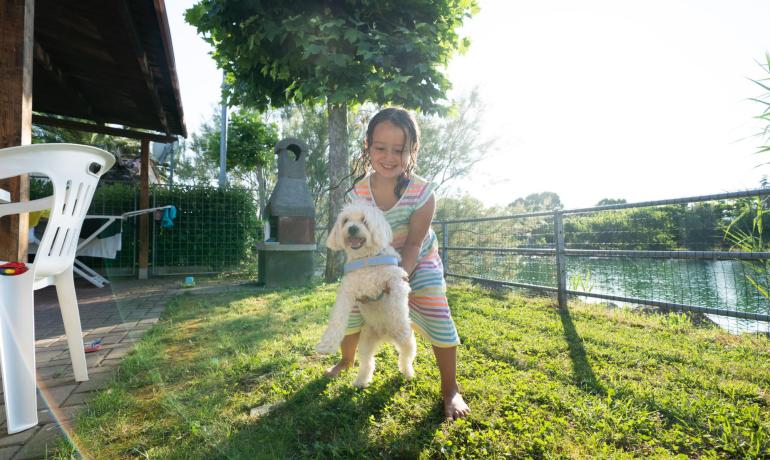 Bambina felice gioca con un cane in giardino soleggiato.